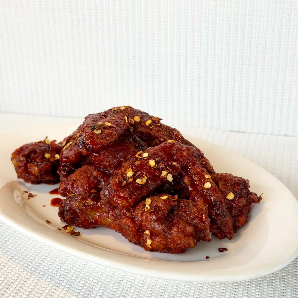 A plate of NamNam Buffalo wings glazed deep red with chili flakes