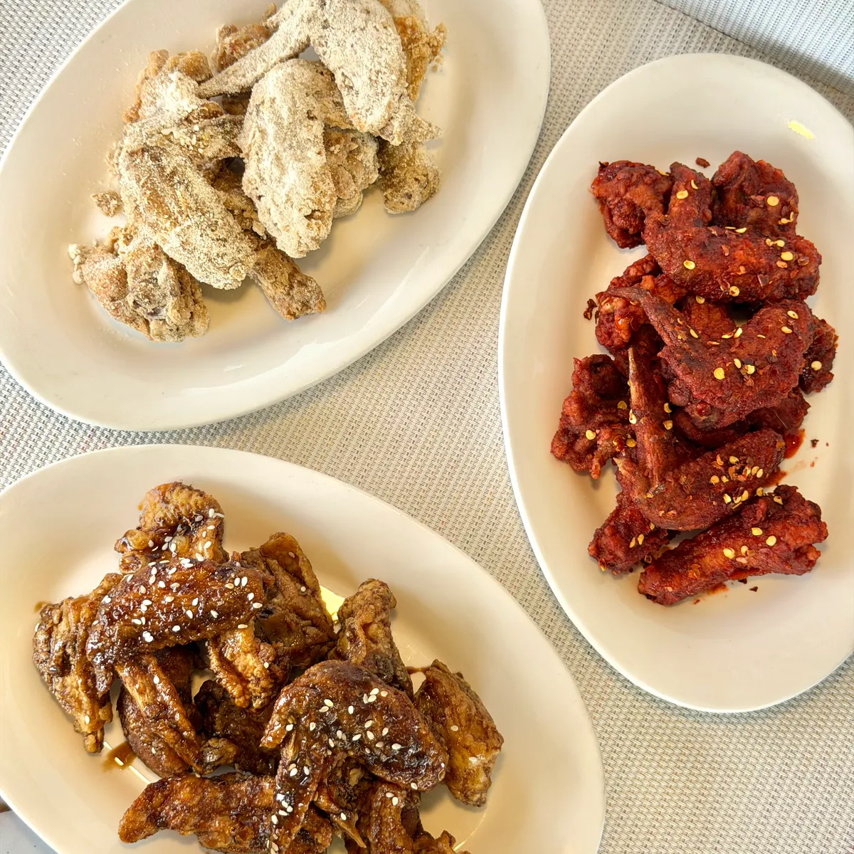 Three platters of NamNam flavored chicken with golden, red-glazed, and sesame-topped pieces
